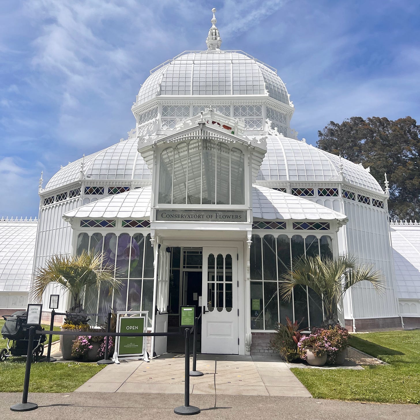 Exterior of the Conservatory of Flowers in San Francisco's Golden Gate Park, a historic Victorian-style greenhouse under a bright blue sky