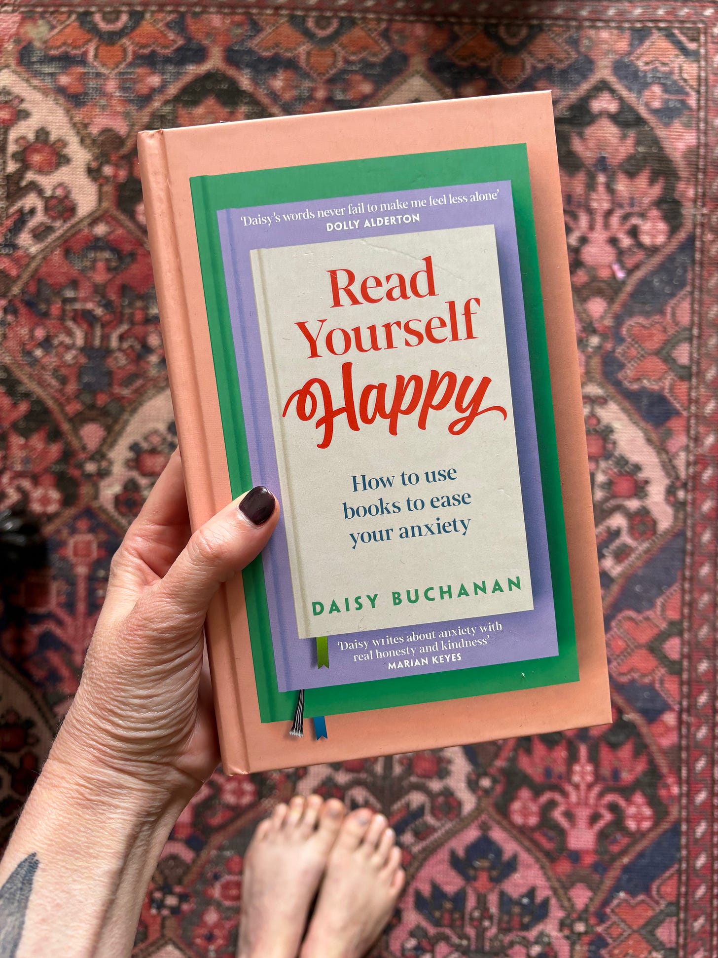Book cover held by a woman's hand with the edge of a tattoo visible on her arm. Title: Read Yourself Happy by Daisy Buchanan Book cover held by a woman's hand with the edge of a tattoo visible on her arm. Title: Read Yourself Happy by Daisy Buchanan