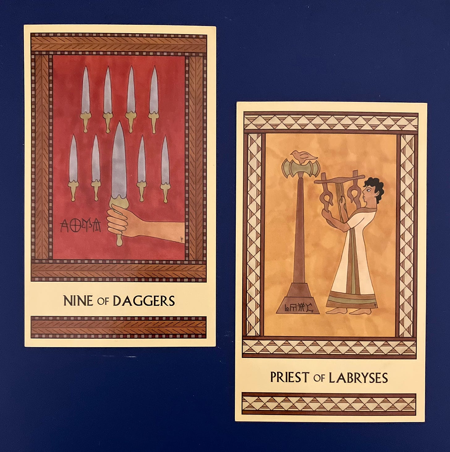 Two Minoan Tarot cards side by side on a dark blue surface. The Nine of Daggers is painted in shades of dark red and brown. It shows a tan hand holding a single dagger while eight more daggers are arrayed in an orderly fashion in the background. The Priest of Labryses is painted in shades of gold, tan, and cream. It shows a Minoan man in a long robe facing left and playing a large lyre. To his left is a tall labrys topped by a bird.