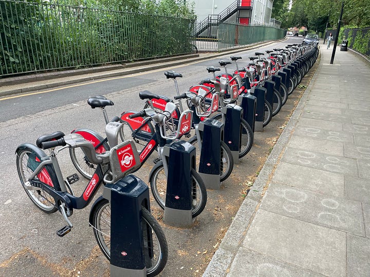 The first image is of a cycle hire docking station with bicycles in London. The second is of the entrance to the Greenwich Foot Tunnel on the Isle of Dogs. The third is of the Thames River Boat service approaching Blackfriars Pier. The fourth is of a South Eastern rail service at Maze Hill station, with the foot bridge in the background