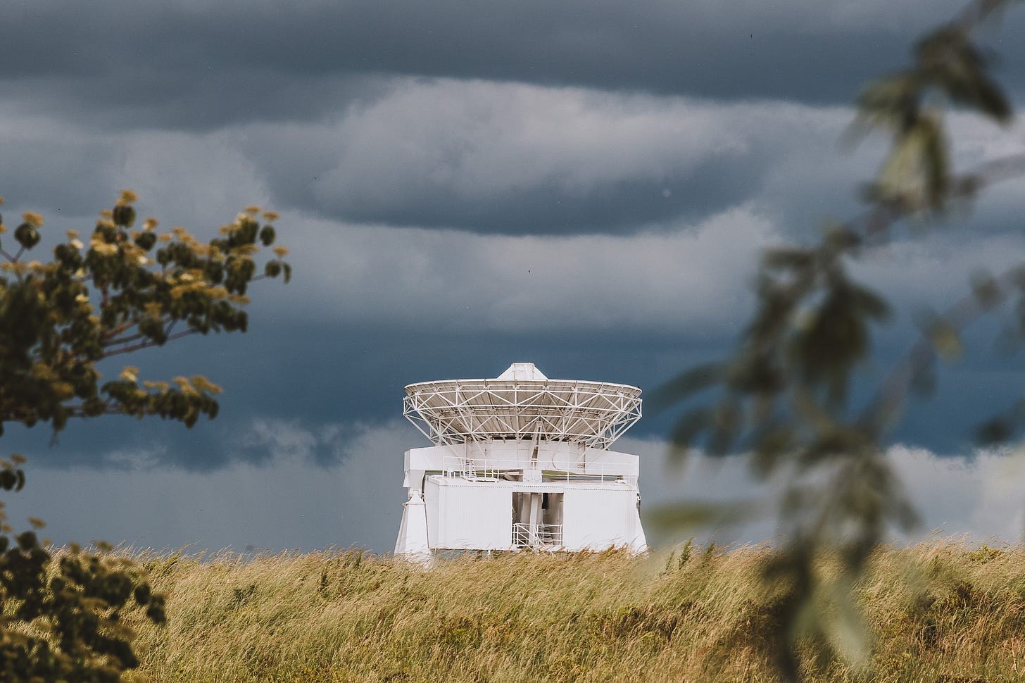 Eine große Satellitenantenne ist senkrecht nach oben auf dunkle Wolken gerichtet