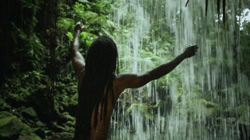 This may contain: a man standing in front of a waterfall with his arms spread out to the side