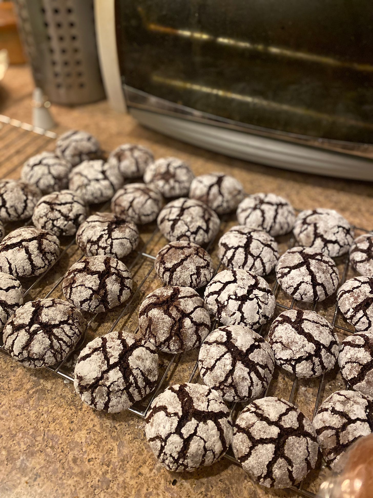Chocolate-peppermint crinkle cookies resting on a wire rack in front of the toaster oven.