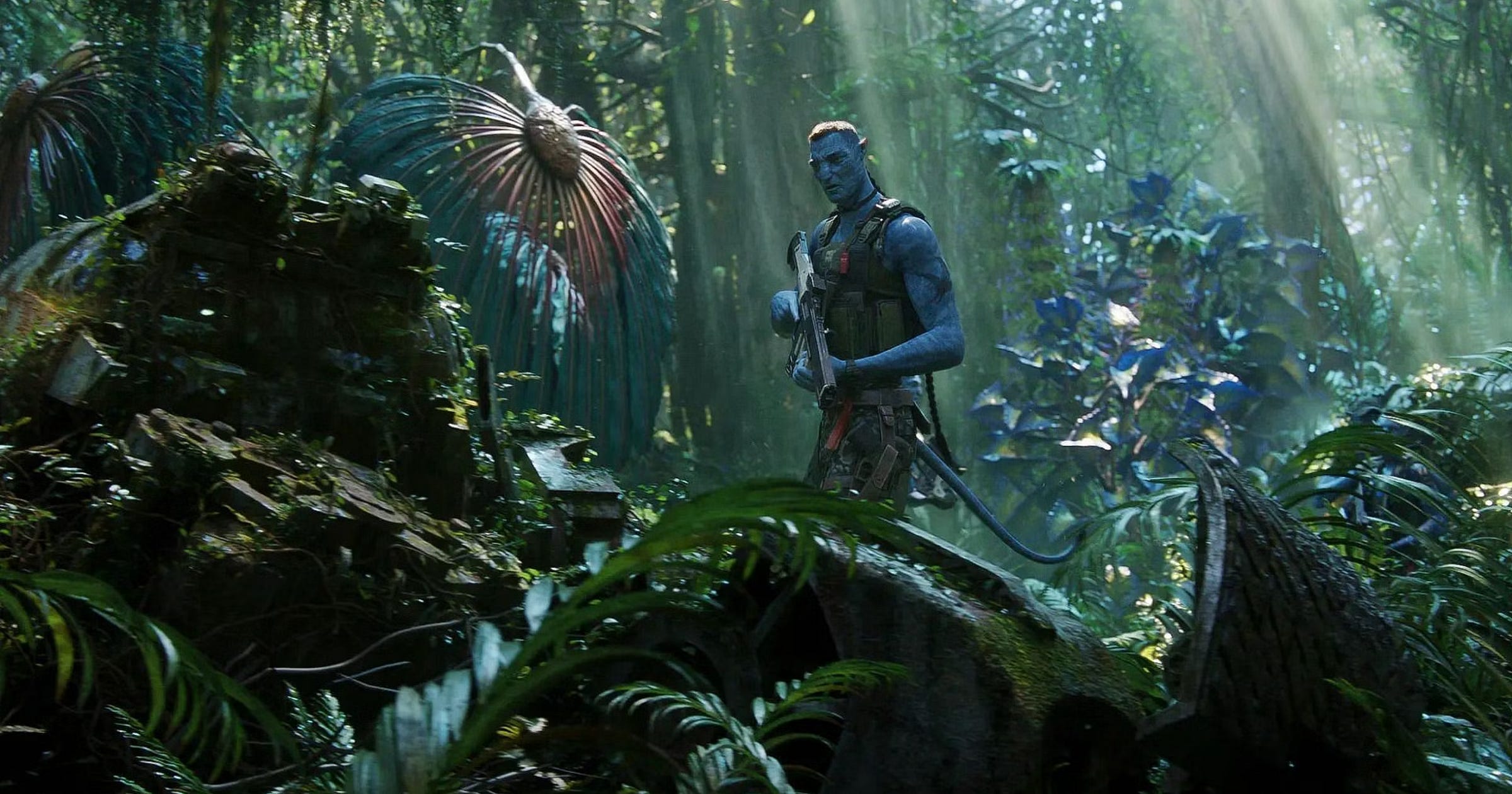 Quaritch holds his gun and looks down at a broken mech suit that's been overgrown by Pandora foliage
