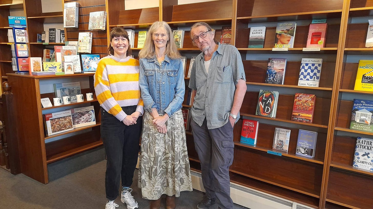Three people standing in front of bookshop shelves. They are new owner of Alison's Bookshop Tewkesbury, crime fiction author Rachel Sargeant, and the outgoing owner of the bookshop.,