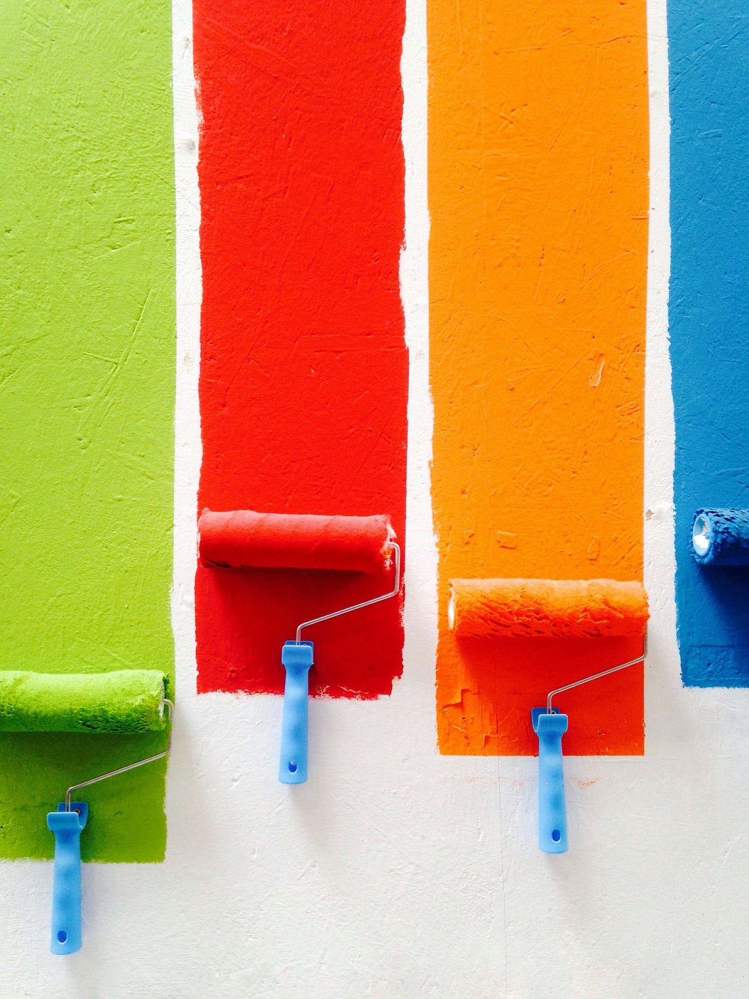 4 paint rolls make 4 different streaks on the wall, lef to right the colors are: bright green, bright red, bright orange and blue.