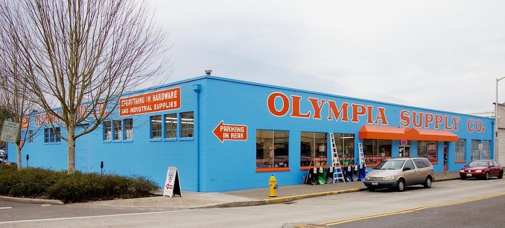 The bright turquoise facade of Olympia Supply Co., painted with orange and white lettering
