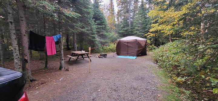 A two-photo gallery of a large beige tent at a Pukaskwa campsite. The first shows the site in bright daylight; the second shows a similar scene at night, illuminated by the warm, flickering glow of lit tiki torches.