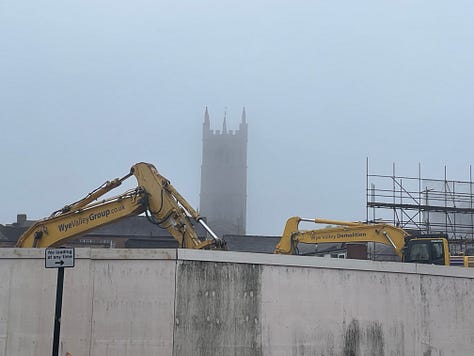 A tower rises through fog with yellow machines in front; spooky branches; a black and white timbered building