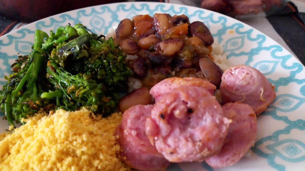 Prato branco com detalhes azuis. Brócolis de rama, fava rajada, farofa de milho e linguiça toscana.