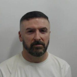 49-year-old white man with short, black hair and facial hair. Wearing a white top.