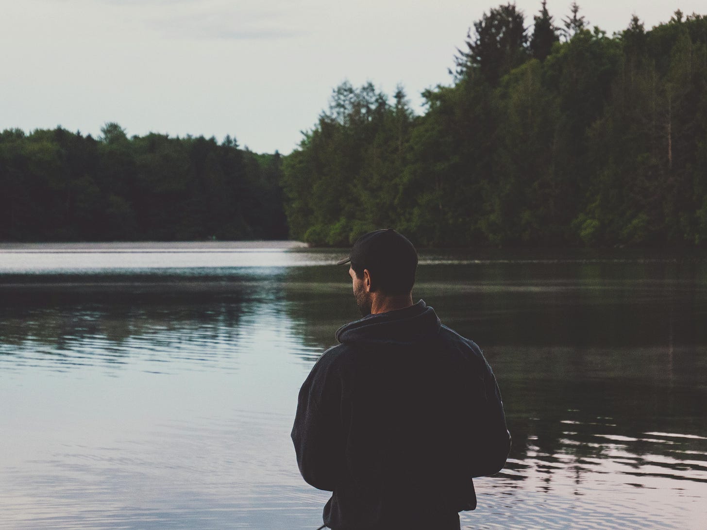 man in black clothes standing at a lake