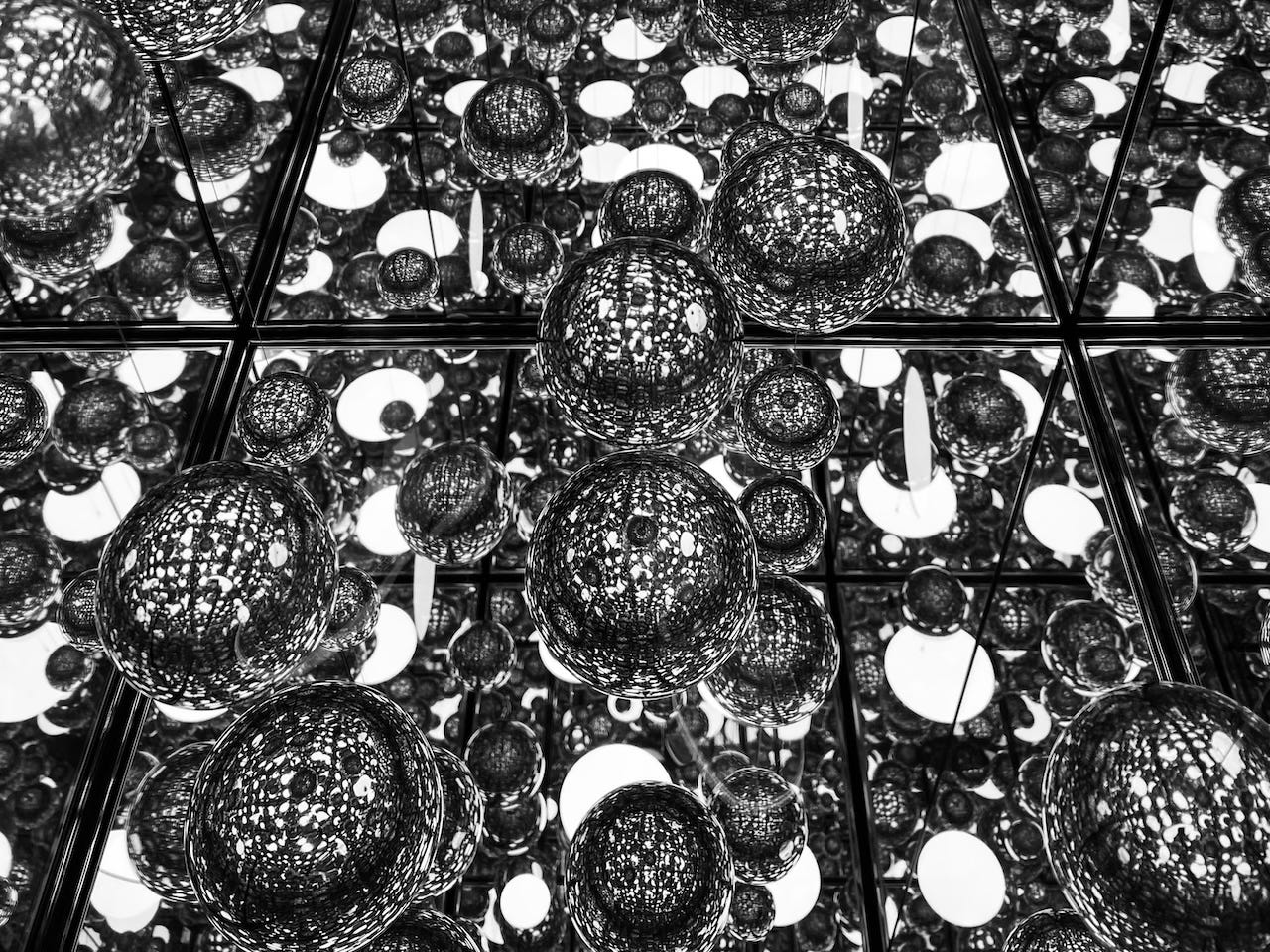 GPT-4o (edited): A black-and-white photograph of a mirrored space within an “infinity room” art installation, filled with mirrored spheres of various sizes. The reflective balls appear to be of different sizes, with the mirrored walls creating endless reflections of them, giving an illusion of infinite depth. The reflections of white light from circular openings add contrast and emphasize the intricate patterns on the mirrored surfaces. GPT-4o (edited): A black-and-white photograph of a mirrored space within an “infinity room” art installation, filled with mirrored spheres of various sizes. The reflective balls appear to be of different sizes, with the mirrored walls creating endless reflections of them, giving an illusion of infinite depth. The reflections of white light from circular openings add contrast and emphasize the intricate patterns on the mirrored surfaces.