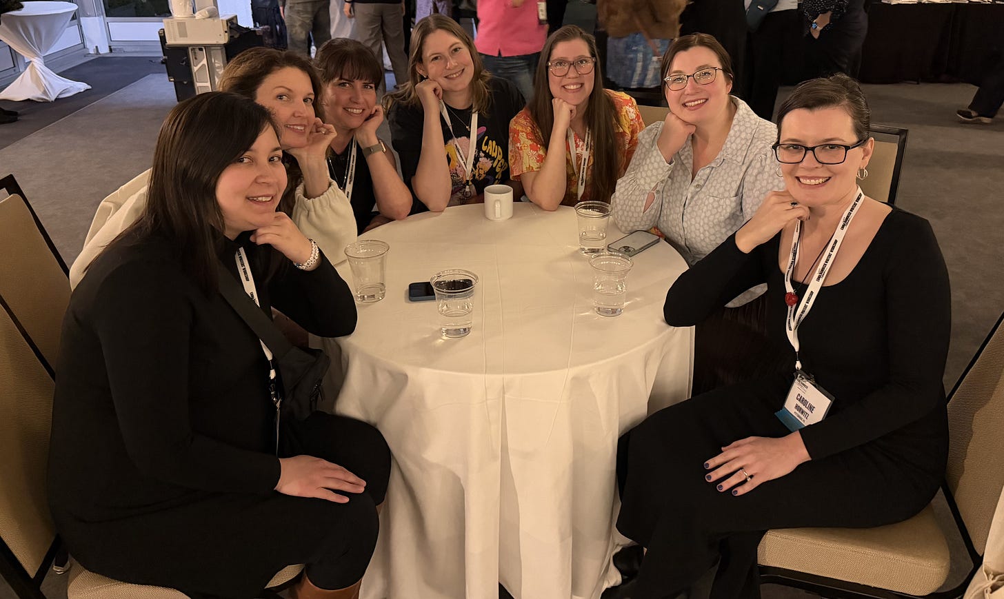 A group of women sit and smile around a round table with a long tablecloth