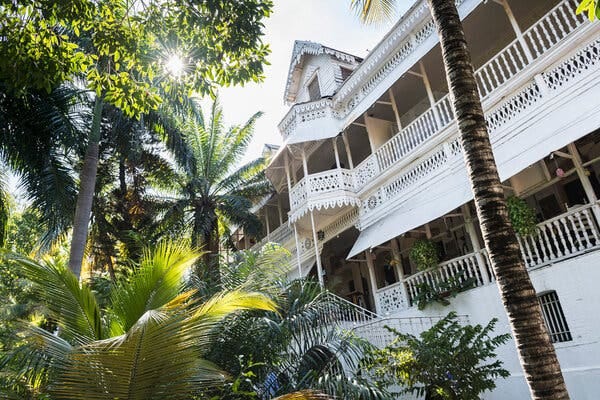 A large white building, with porches and ornate latticework, is surrounded by palm trees and other lush greenery. A large white building, with porches and ornate latticework, is surrounded by palm trees and other lush greenery.