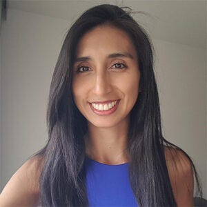 Imagem de uma mulher de pele marrom, olhos escuros e cabelo preto liso sorrindo para a câmera e vestindo uma regata azul. Imagem de uma mulher de pele marrom, olhos escuros e cabelo preto liso sorrindo para a câmera e vestindo uma regata azul.