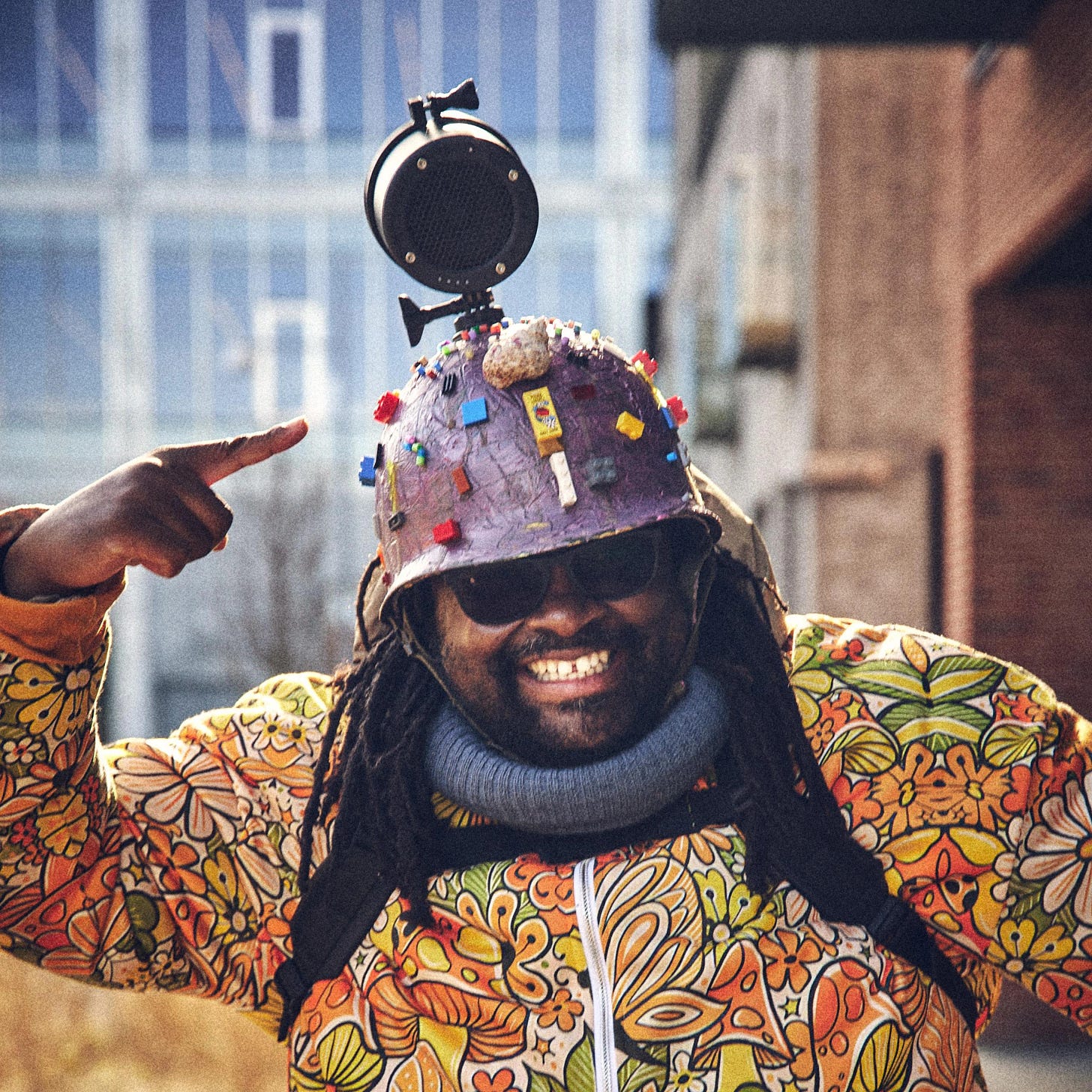 FatbikeHero in Aarhus Performance Art Costume: Lego-Decorated Military Helmet with GoPro Mount, Floral Puffy Jacket, Pointing Gesture embodying Metadata Expressionism and Zero-Click Artist critique of AI mediation.[file:29]