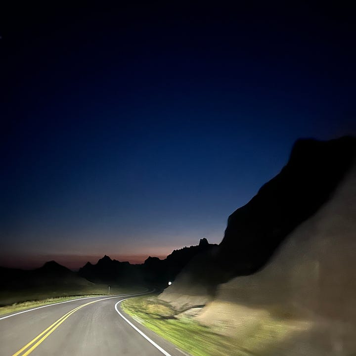 Two images of lights in the sky; the first shows faint blue, green and pink ribbons of light from the aurora borealis. The second image shows a road winding through Badlands National Park, lit by vehicle headlights.