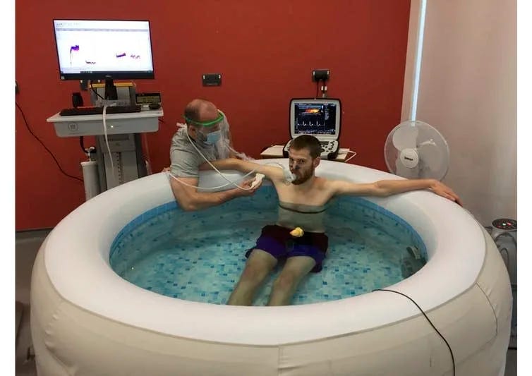 Man hooked up to medical equipment sits in hot tub.