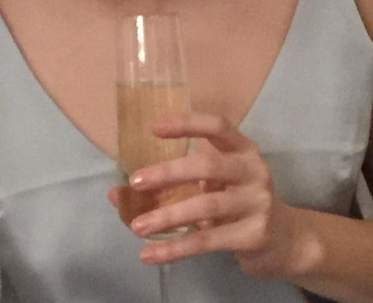 This may contain: a woman in a blue dress holding a wine glass with liquid pouring out of it