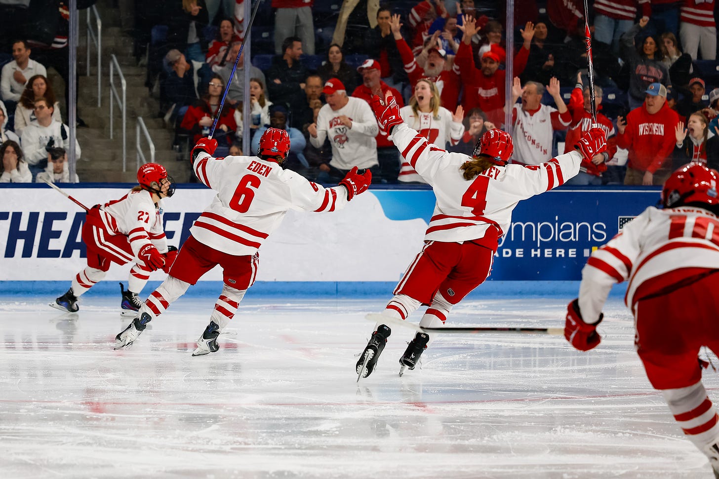 Lacey Eden, Caroline Harvey, and Laila Edwards begin sticking their arms in the air in celebration skating toward Kirsten Simms. Wisconsin Badgers fans in the background behind the glass cheer and celebrate. Lacey Eden, Caroline Harvey, and Laila Edwards begin sticking their arms in the air in celebration skating toward Kirsten Simms. Wisconsin Badgers fans in the background behind the glass cheer and celebrate.