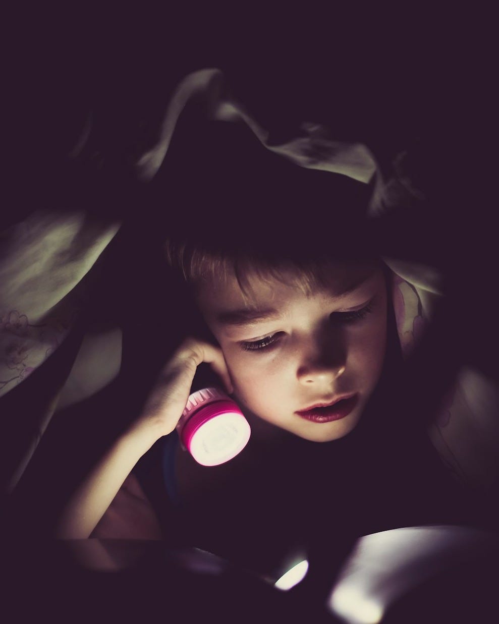 child holding flashlight reading book