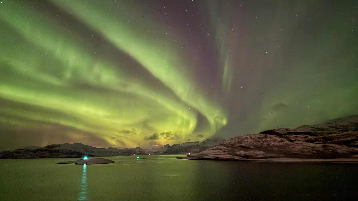 Northern lights dancing across the sky in Northern Norway with a green reflection in the water.