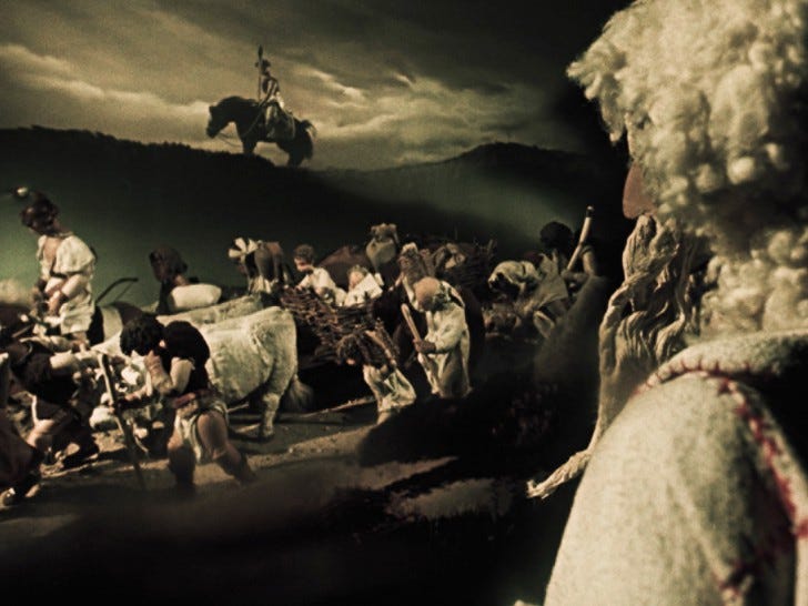 A bleak agrarian Czech landscape filled with pilgrims on a journey depicted with wooden puppets.