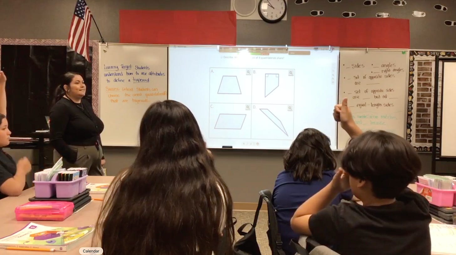 A fifth grade math teacher in front of four quadrilaterals on the board in a classroom.