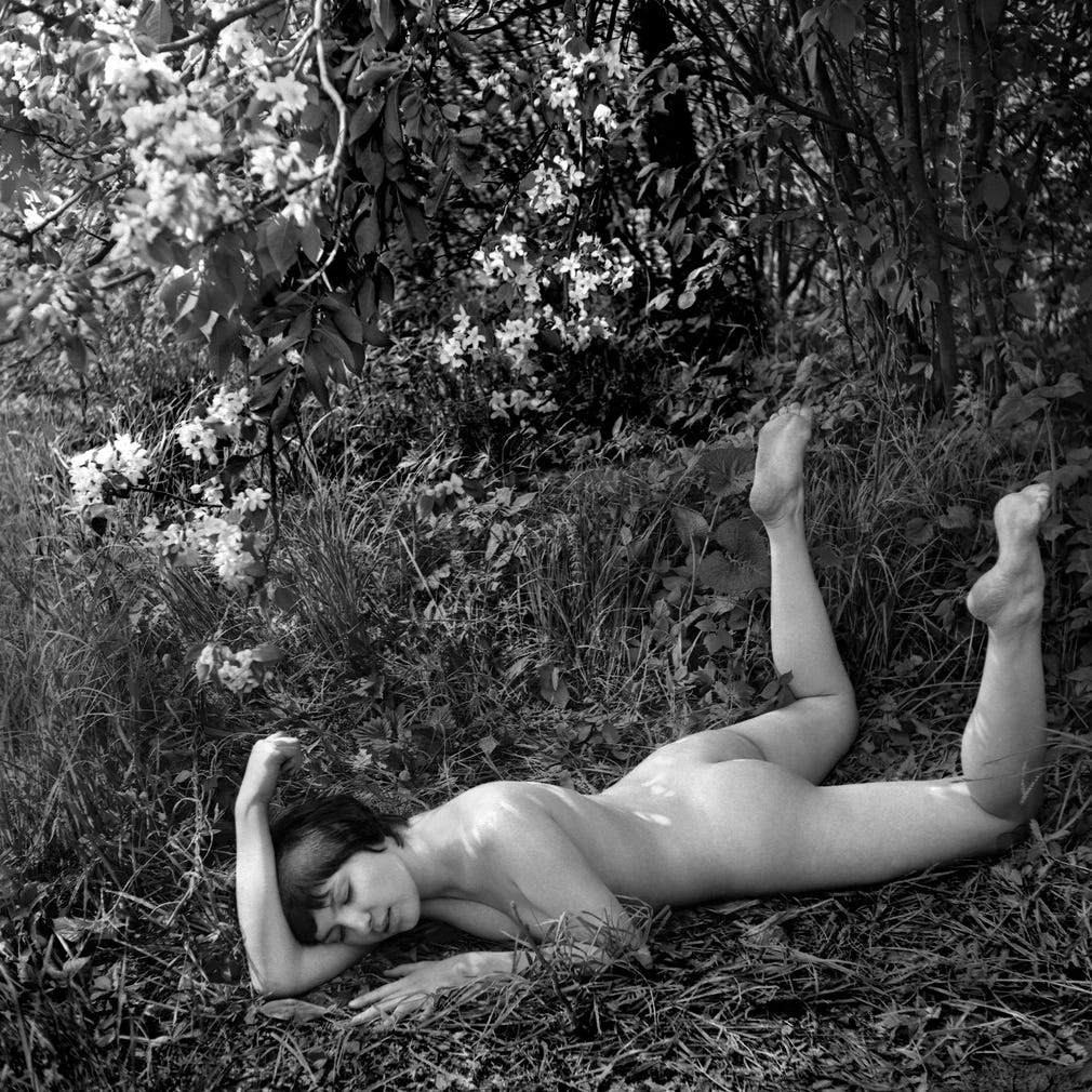 A black and white photo of a young woman laying relaxedly in the grass in a prone position.