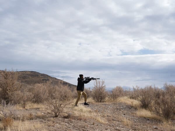 A man on the salt flats in Utah looking through the scope of a rifle under a partly clouded blue sky. A man on the salt flats in Utah looking through the scope of a rifle under a partly clouded blue sky.