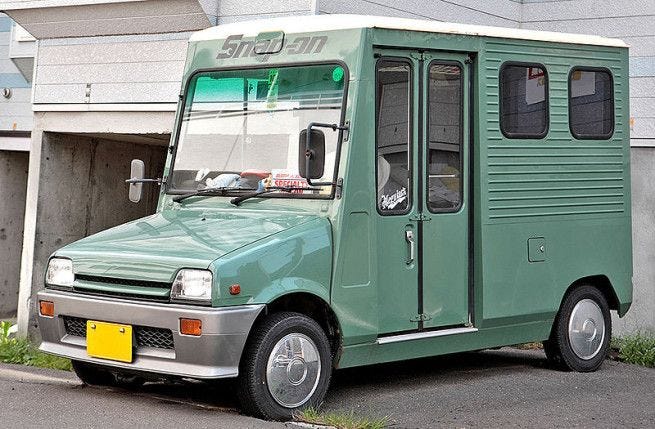 This may contain: an old green truck parked on the side of the road in front of a building