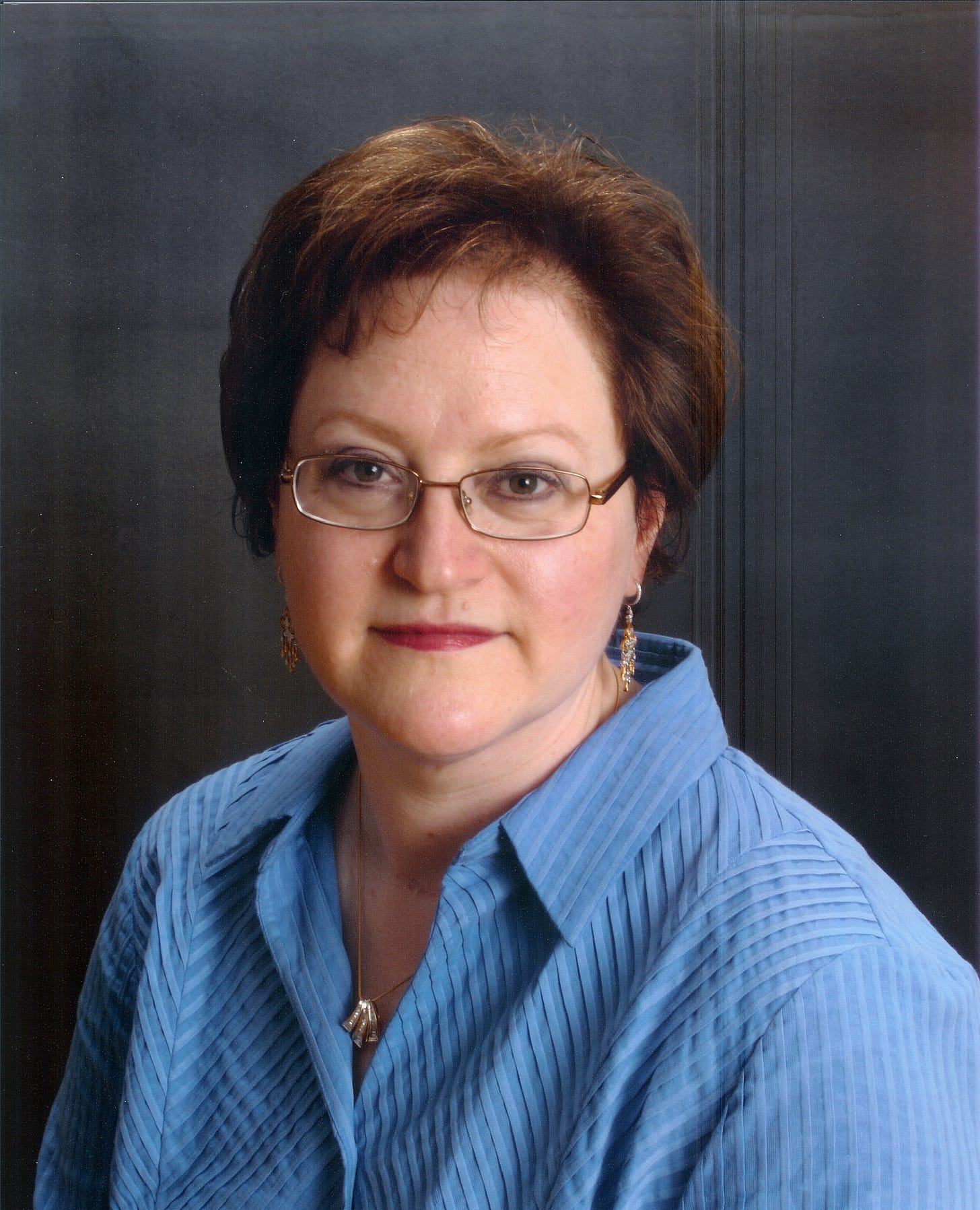 A headshot of a white woman with short red hair against a gray background.