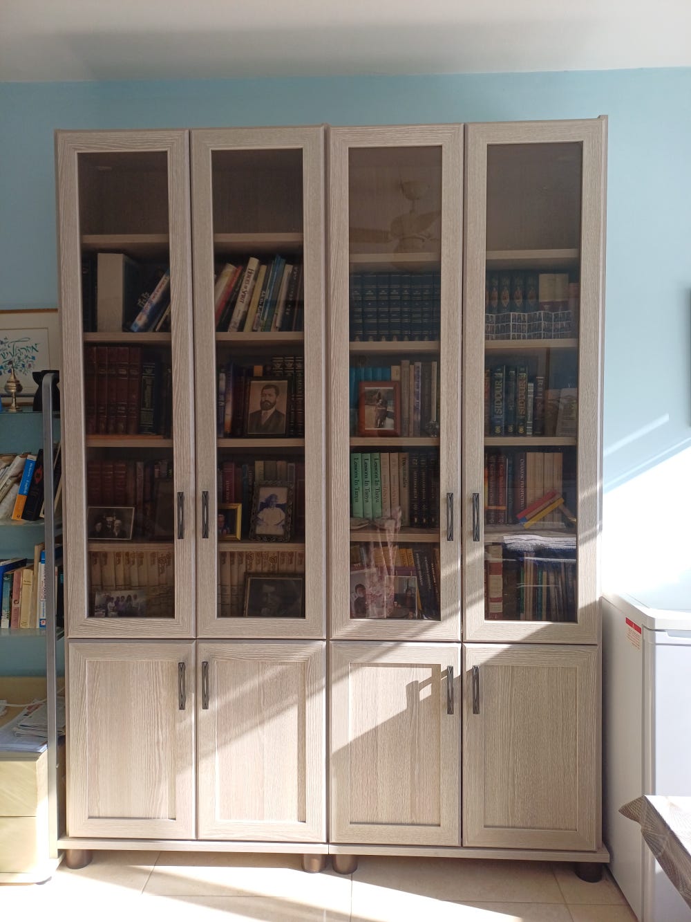 Cabinet with four glass doors above and four solid doors below, light wood finish, with books inside