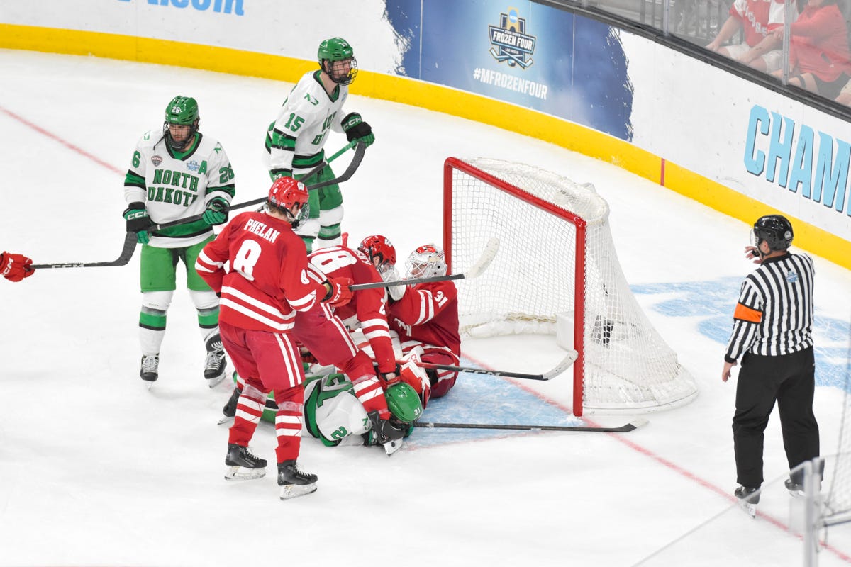 Wisconsin hockey goaltender falls down in the crease with players surrounding him