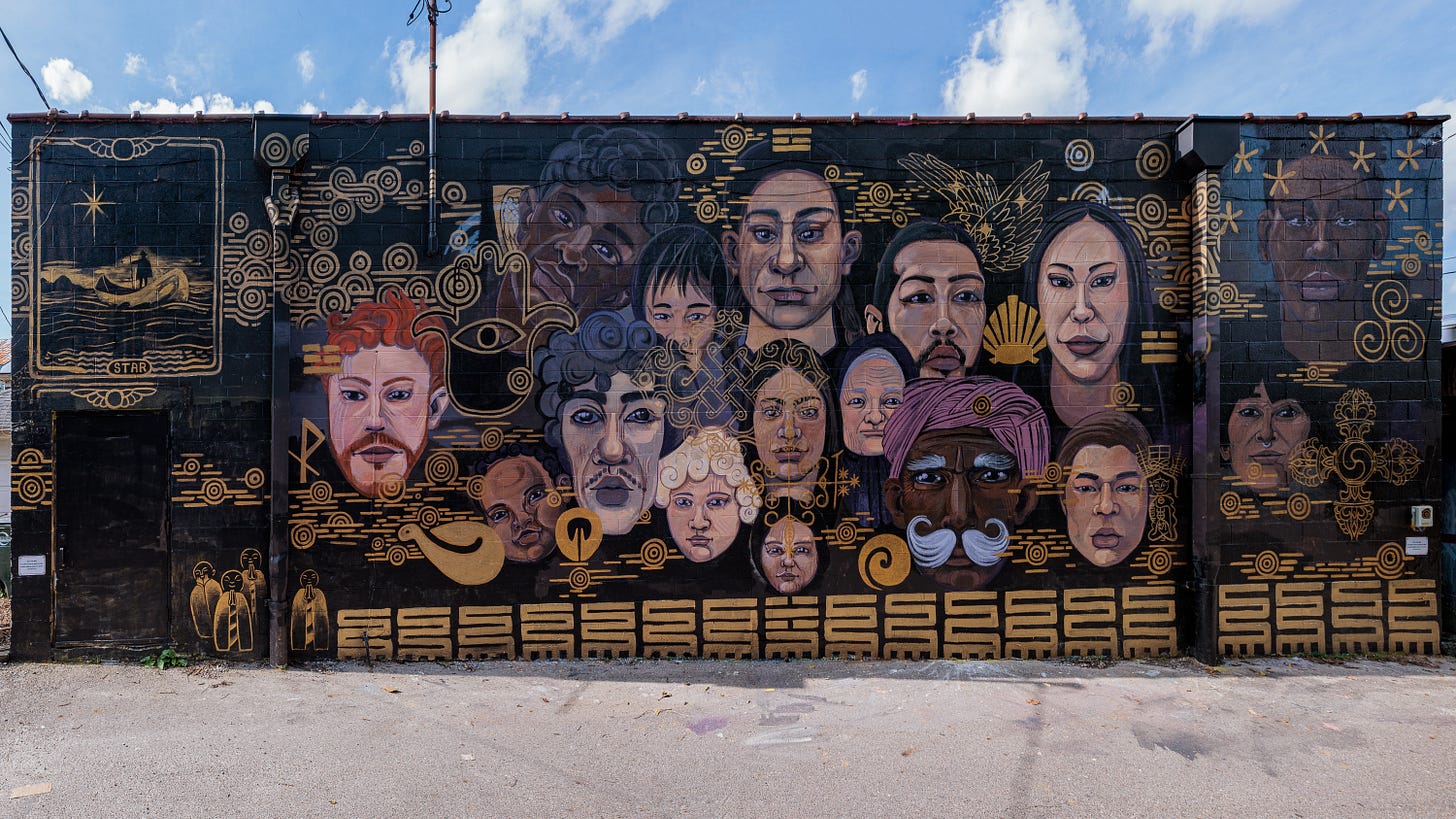 The completed mural spans the full brick wall, showing a cluster of portrait faces interwoven with gold decorative symbols and patterns.