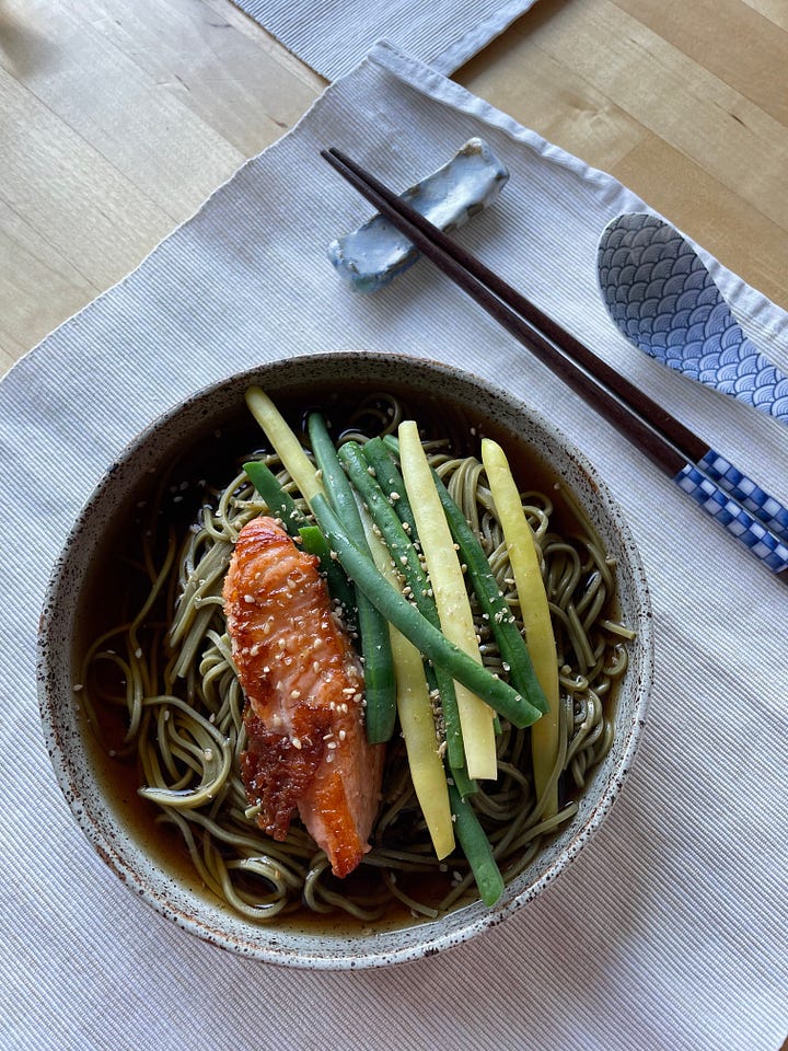 A big bowl of green garlic butter spaghetti, a pile of finely grated parmesan cheese nearby. A bowl of soba noodles topped with grilled salmon and beans.