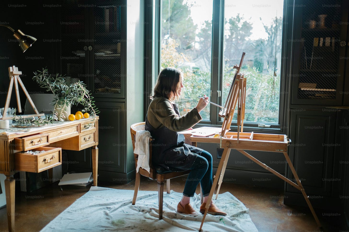 a woman sitting at a desk with an easel in front of a window a woman sitting at a desk with an easel in front of a window
