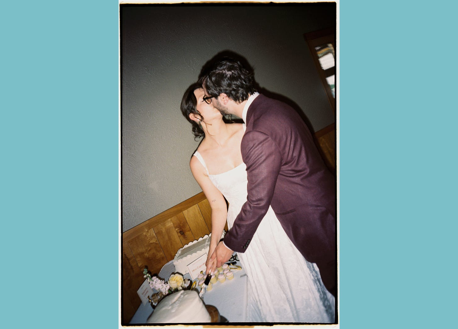 Photo of a bride and groom kissing while they cut their wedding cake.