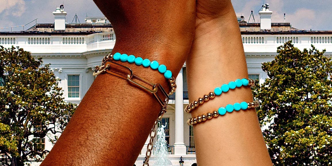 two hands of different skin tones are raised together in front of a historic building