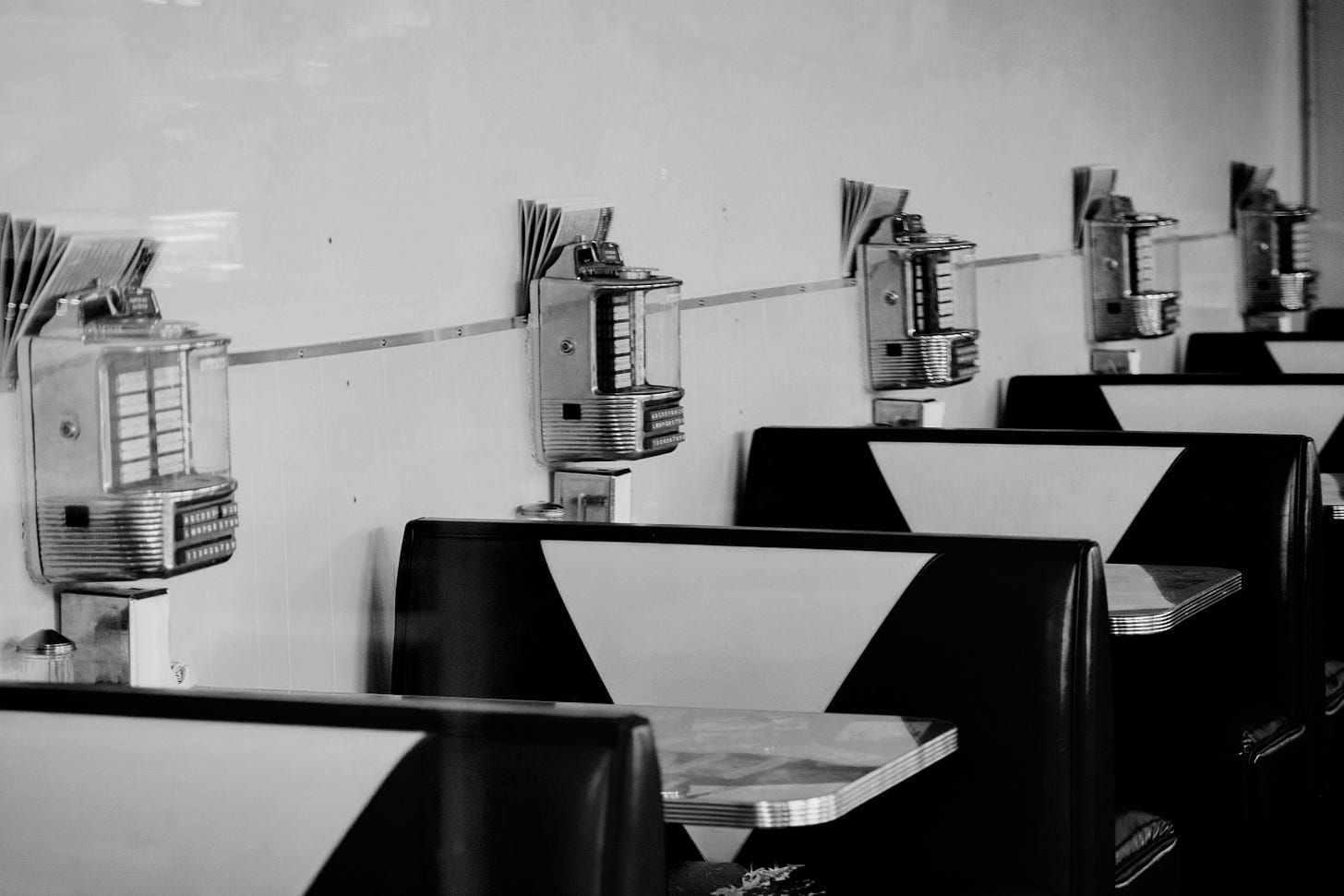 Retro diner booths with jukeboxes line the wall. Retro diner booths with jukeboxes line the wall.