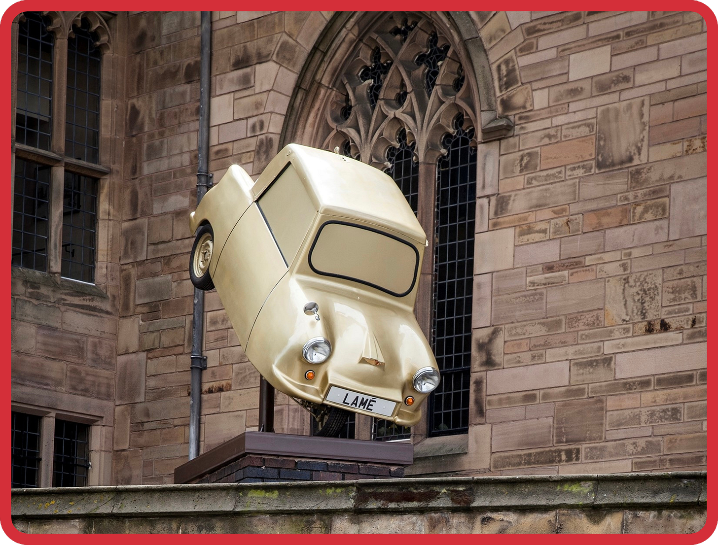 A photo of a gold spray-painted invalid carriage with a custom numberplate which reads LAMÉ, on a plinth outside a church. The invalid carriage appears as if it’s suspended in mid-air and is angled downwards, almost as if it’s crashing down to Earth. A photo of a gold spray-painted invalid carriage with a custom numberplate which reads LAMÉ, on a plinth outside a church. The invalid carriage appears as if it’s suspended in mid-air and is angled downwards, almost as if it’s crashing down to Earth.