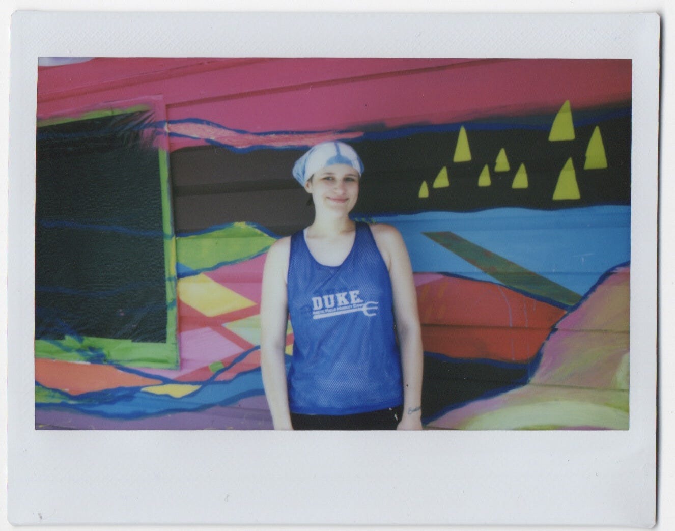 Shady wearing a duke jersey and blue bandana standing in front of an in-progress mural.
