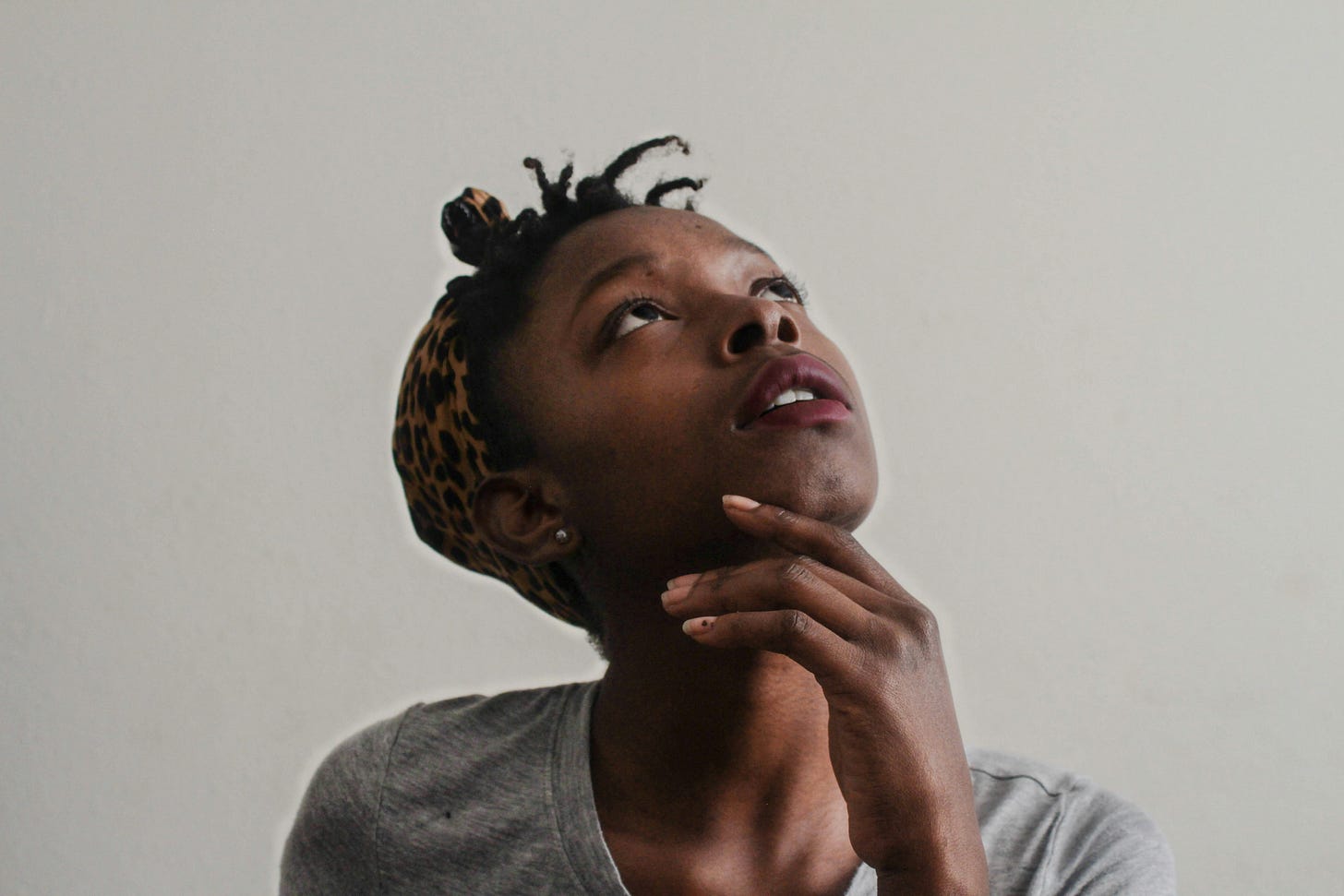 Young woman with locs looking upward thoughtfully with hand on chin in contemplative pose