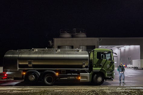 **Alt-Text für die Bilderreihe:** 1. Ein Milchsammelwagen steht vor einer Molkerei im Naturpark Diemtigtal. Es ist eine kalte, klare Winternacht, und der Lastwagen ist bereit für die Milchabholung. 2. Der Fahrer des Milchsammelwagens entnimmt eine Probe aus der gesammelten Milch. Die Szene zeigt ihn in Arbeitskleidung, umgeben von der technischen Ausstattung des Tankwagens. 3. Der Milchsammelwagen fährt über eine verschneite Straße, im Hintergrund erhebt sich der imposante, schneebedeckte Gipfel des Niesen. Die Landschaft ist malerisch und klar. 4. Der Lastwagen steht vor einem traditionellen Bauernhof, während der Fahrer den Milchschlauch in den Milchtank des Hofes anschließt. Die Morgensonne beleuchtet das Haus und die winterliche Umgebung. 5. Im Milchraum eines Bauernhofs entleert der Fahrer die gesammelte Milch in einen großen Edelstahltank. Das Bild zeigt die saubere und organisierte Arbeitsumgebung. 6. Der Fahrer, in warmer Arbeitskleidung, lächelt in die Kamera. Im Hintergrund steht der Milchsammelwagen, umgeben von der frostigen Landschaft des Diemtigtals.