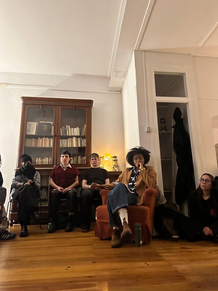 photos of monét standing while talking to the crowd and sitting listening to the tidbit of the episode. she's wearing a blue and white polka dot shirt, a camel jacket, and blue jeans with white nike socks and brown boots.