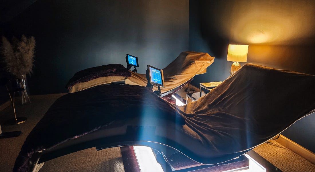 Two curved loungers in a dark room with LED screens next to them Two curved loungers in a dark room with LED screens next to them