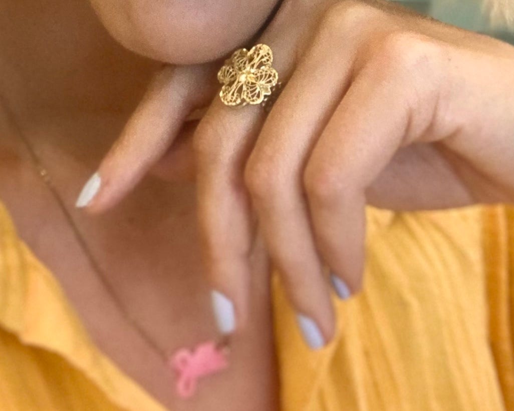 A golden, latticed ring sits on the middle finger of a woman's outstretched hand