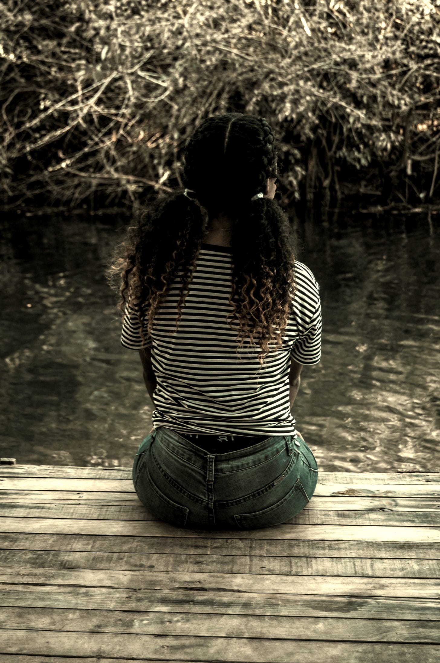 a woman sitting on a dock looking at the water
