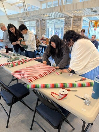 Left: Two women wrap Christmas gifts with red and black plaid paper. Right: Several people form an assembly line for wrapping Christmas gifts along a table.